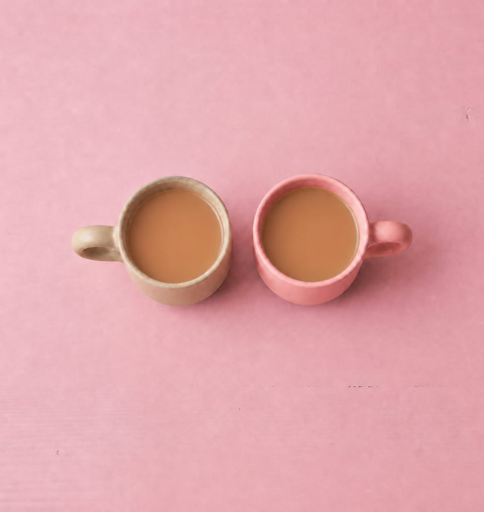 Two mugs of tea on a pink surface